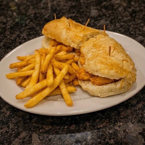 Cajun fried chicken po'boy sandwiches with french fries on a white plate.