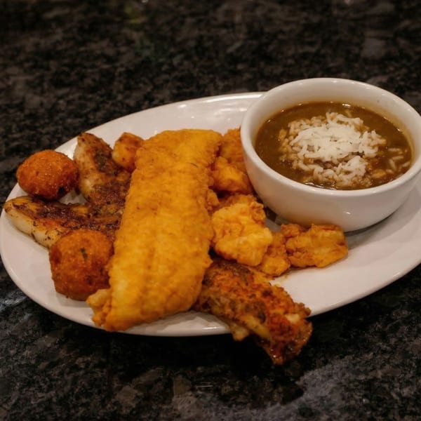 A white plate with fried fish, hush puppies, and a bowl of gumbo with rice.