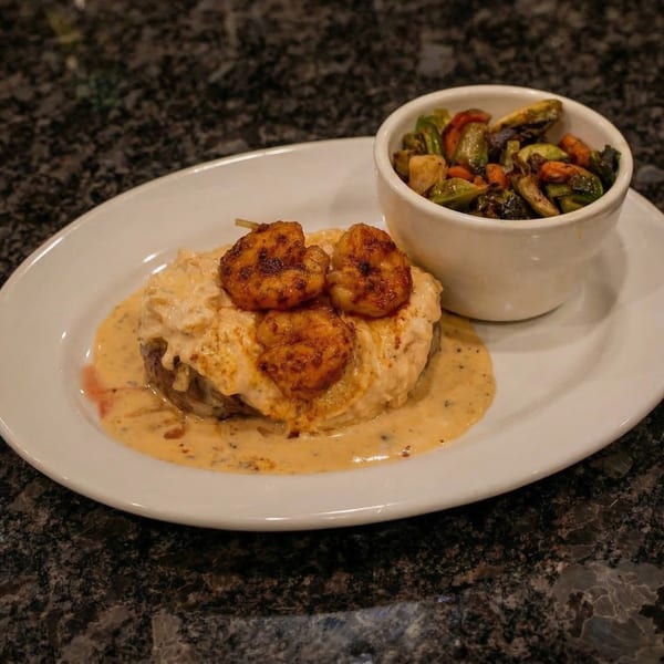 Cajun steak with creamy sauce and grilled shrimp, served with a side of roasted vegetables.