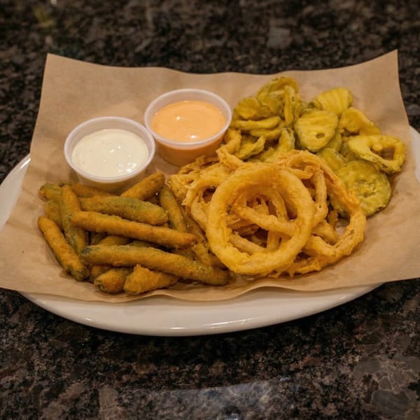 A platter of fried green beans, onion rings, and pickles with two dipping sauces.