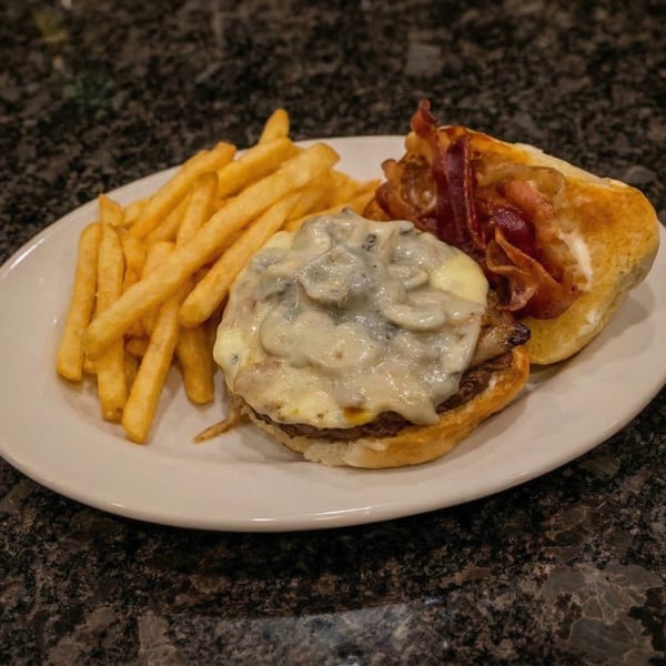 A T-Doug's Cajun Cuisine burger with mushroom sauce, bacon, and fries on a white plate.